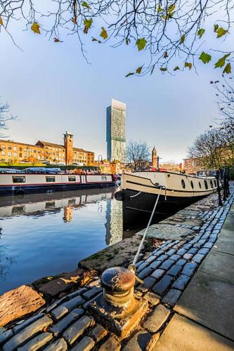 曼彻斯特Minimalist space - Manchester City Centre的船停靠在河上,船屋背景是建筑
