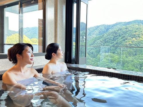 伊东加兰考特宇佐美私人温泉公寓式酒店的两名女性坐在热水浴缸中,享有美景