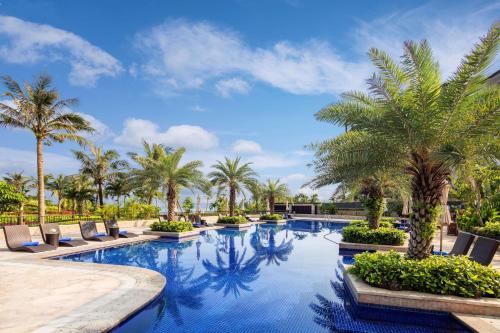 文昌文昌鲁能希尔顿酒店的一个带棕榈树和躺椅的游泳池