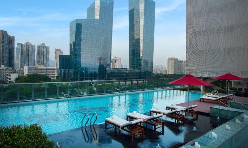 深圳深圳大中华希尔顿酒店（地铁出站即达、近福田会展中心）的一座大楼内的游泳池,配有椅子和遮阳伞