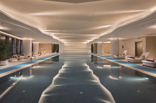 沈阳沈阳世茂希尔顿酒店的酒店大堂设有一座带白色椅子的游泳池