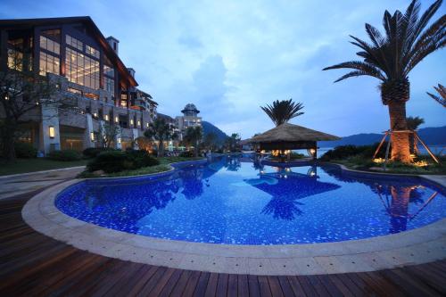 淳安千岛湖滨江希尔顿度假酒店的一座种植了棕榈树的大型蓝色泳池和一座建筑