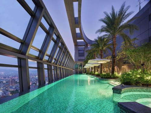 台北台北新板希尔顿酒店的棕榈树建筑中间的游泳池