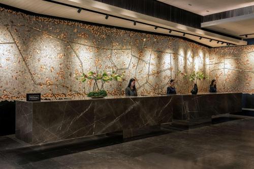 曼谷曼谷奔集路希尔顿逸林酒店的三个妇女站在墙上,墙上有植物