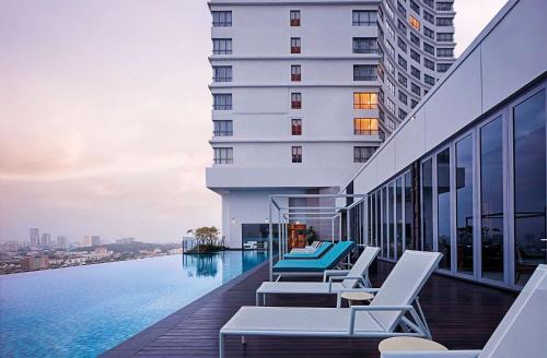 马六甲马六甲希尔顿逸林酒店的酒店游泳池设有躺椅,酒店大楼