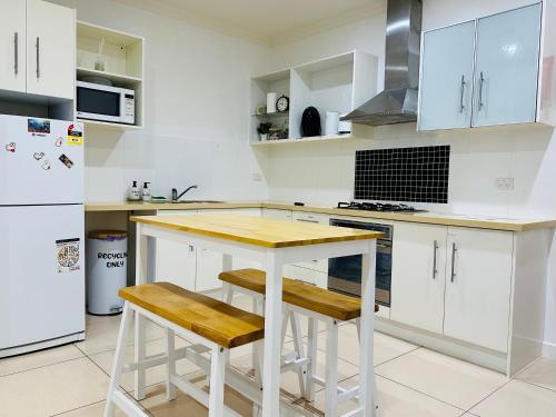 阿德莱德Bundled Bliss 2 bedroom Condo in Adelaide CBD的厨房配有白色橱柜、木桌和凳子