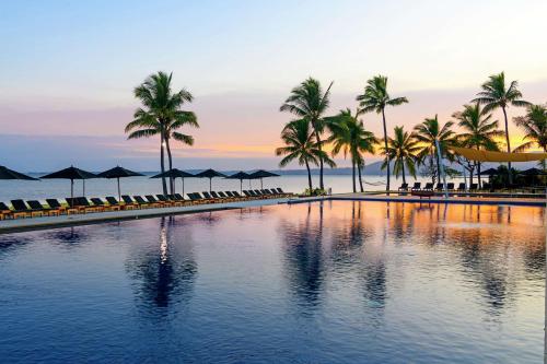 丹娜努斐济海滩希尔顿度假酒店的棕榈树和遮阳伞的游泳池以及海洋