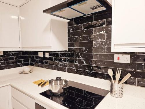 伦敦Wonderful Apartment in Wembley的厨房配有白色橱柜和黑色瓷砖墙