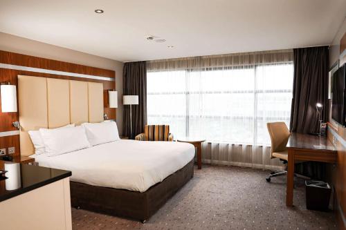 米尔顿凯恩斯希尔顿米尔顿凯恩斯双树酒店的配有一张床、一张书桌和一扇窗户的酒店客房