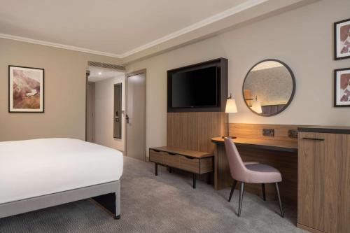达特福德达特福德大桥希尔顿逸林酒店的一间卧室配有一张床、一张书桌和一台电视。