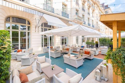凡尔赛Waldorf Astoria Versailles - Trianon Palace的户外庭院配有白色的桌椅和遮阳伞。