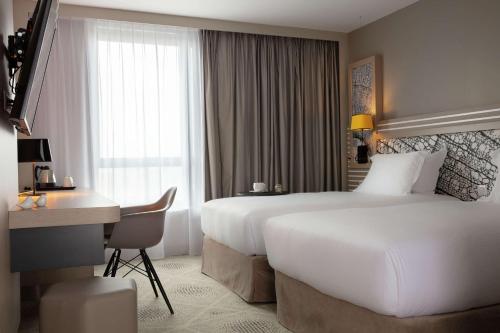 马西Hilton Garden Inn Paris Massy的酒店客房配有两张床和一张书桌