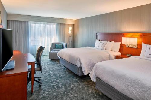 奥尔巴尼Courtyard by Marriott Albany Thruway的酒店客房设有两张床、一张桌子和一台电视。