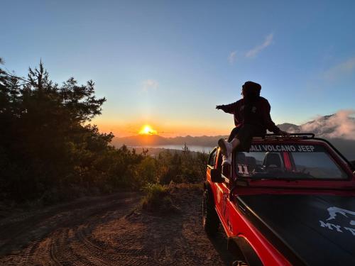 库布盼洛坎La Collina Glamping Cabin的坐在汽车顶上,在土路上,欣赏日落的人