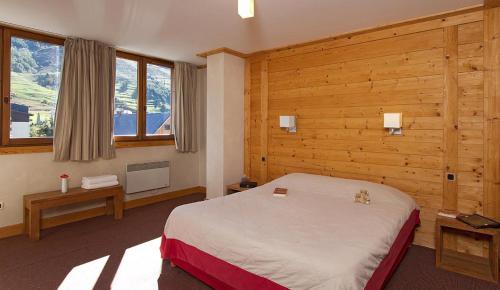 莱德萨阿尔卑斯Vacancéole - Résidence Cortina的一间卧室设有一张床、木墙和窗户。