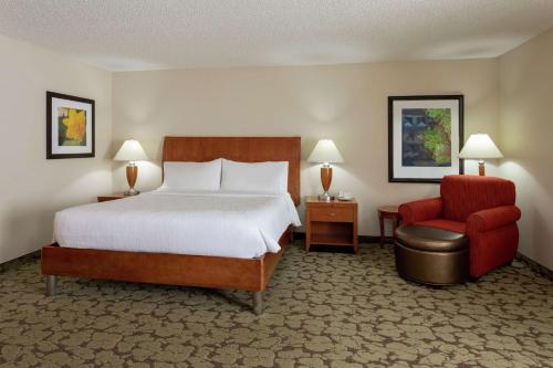 奥克代尔Hilton Garden Inn St. Paul Oakdale的酒店客房,配有一张床和一张红色椅子