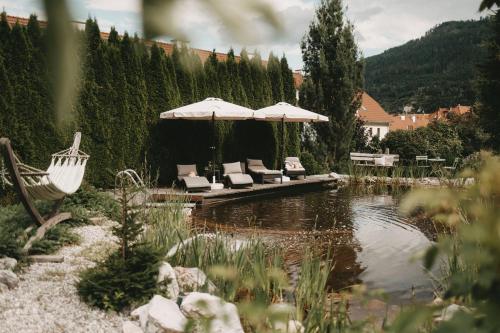 穆劳Hotel Rosenhof Murau的池塘旁的一组椅子和遮阳伞