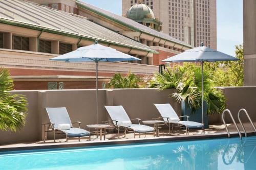 新奥尔良新奥尔良希尔顿逸林酒店的一组椅子和遮阳伞,位于游泳池旁