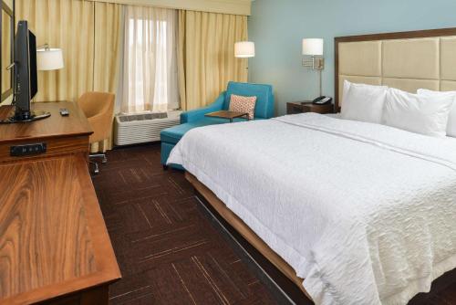 维洛海滩Hampton Inn Vero Beach Outlets的酒店客房带一张床、一台电视和一把椅子