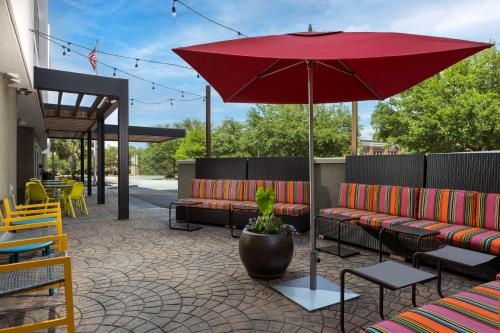 查尔斯顿Home2 Suites by Hilton Charleston Airport Convention Center, SC的一个带红色雨伞、长凳和桌子的庭院