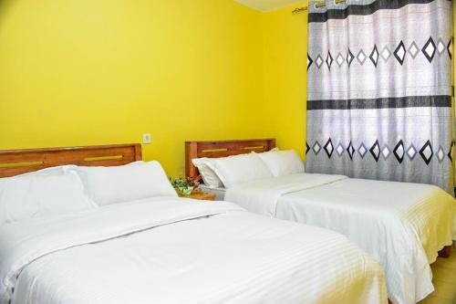 MeruFour seventy的黄色墙壁的客房内设有两张白色的床