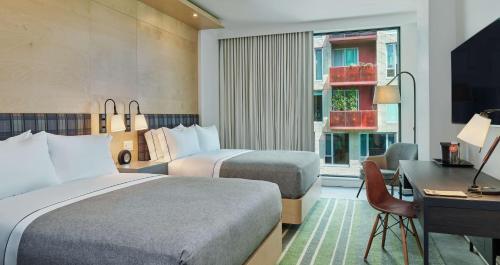 波特兰Canopy by Hilton Portland Pearl District的酒店客房设有两张床、一张书桌和一个窗户。