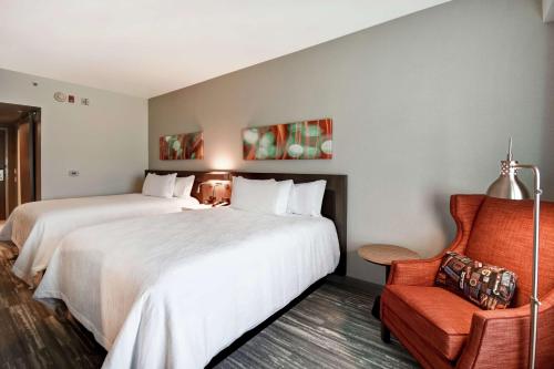 兰辛Hilton Garden Inn Lansing West的酒店客房,配有两张床和椅子