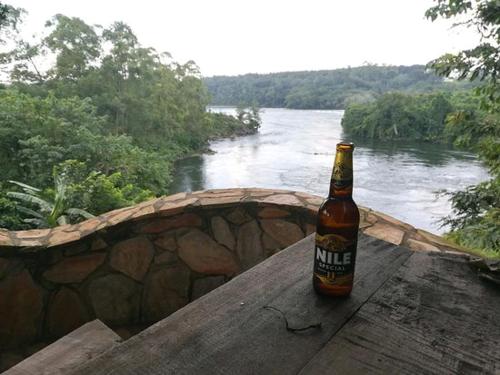 金贾Nileit Campsite Jinja的坐在河边的桌子上,喝一瓶啤酒