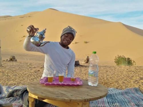 AdrouineGambe Camp的坐在沙漠里,坐在桌子边喝着饮料的人
