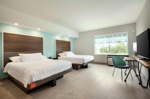 查尔斯湖Tru By Hilton Lake Charles的酒店客房设有两张床、一张桌子和一台电视。