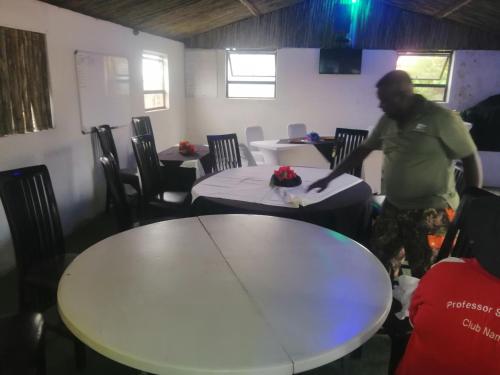 Okahatjipara Lodge的站在带两张桌子的房间的人