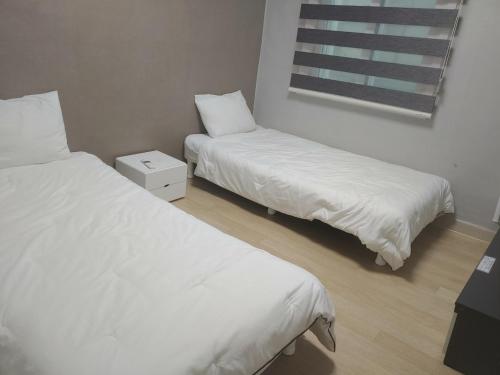 清州市T stay guesthouse的配有白色床单和窗户的客房内的两张床