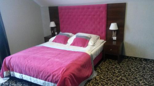 WolanówMaxima Hotel的一张大床,在酒店的房间里设有粉红色床头板
