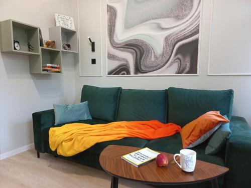 罗兹Przytulne studio przy Atlas Arena i malowniczym parku的绿色长沙发,带橙色毯子和桌子