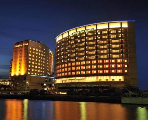 那霸那霸塔度假Spa酒店的水体旁边的一座灯光明亮的酒店大楼