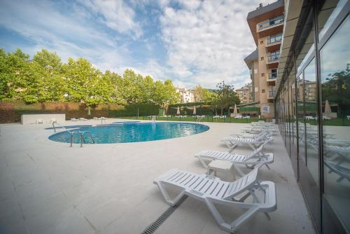 哈卡Oroel Hotel & SPA的一座带白色躺椅的游泳池,位于大楼旁