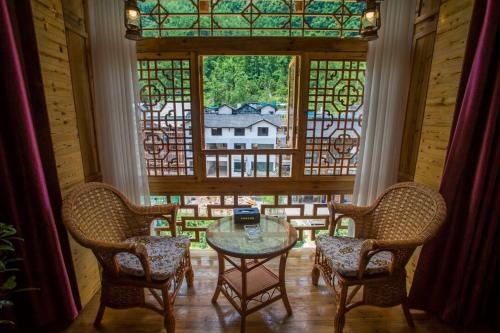 张家界Mountain View Guesthouse的一间设有玻璃桌、两把椅子和窗户的房间