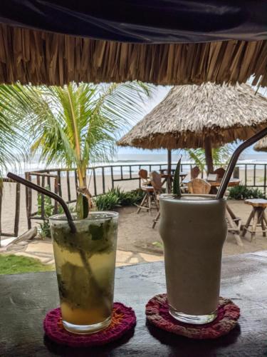 拉斯彭尼塔斯Mano a Mano Eco Hostal的坐在海滩前的桌子上享用2杯鸡尾酒