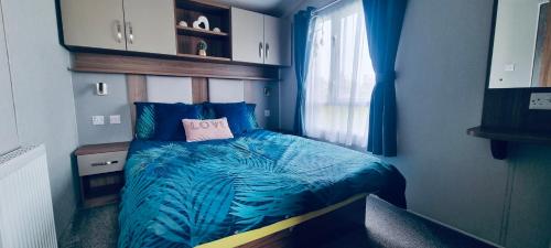 塔特舍尔RJ Luxury Caravan Hire With Hot Tub的一间卧室配有一张带蓝色棉被的床和窗户。