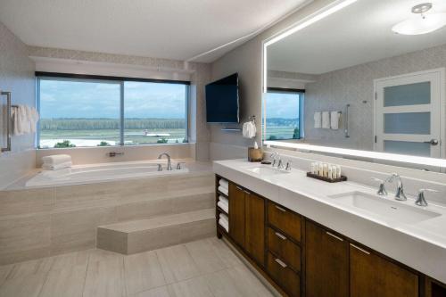 波特兰Embassy Suites by Hilton Portland Airport的一间带两个盥洗盆的浴室和一个带大窗户的浴缸