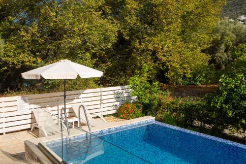 奈德里Zisis Suites的游泳池配有遮阳伞、椅子和带遮阳伞的桌子