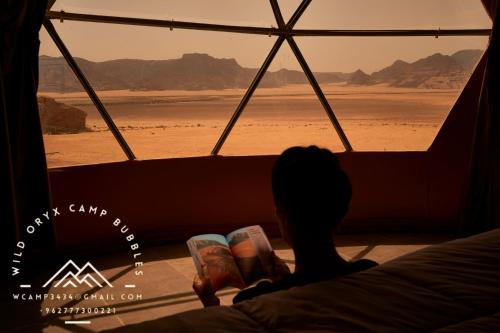 瓦迪拉姆Wild Oryx Camp Bubbles的坐在床上,看着沙漠的窗户的人