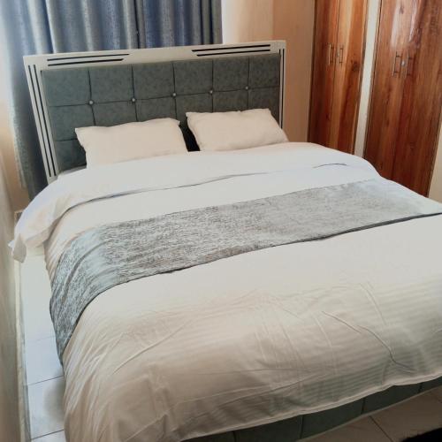 KakamegaMilly's homes的一张带灰色床头板和白色床单及枕头的床