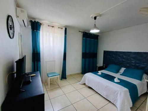 勒拉芒坦COQUET F2 CLIMATISE AVEC PISCINE AU LAMENTIN的一间卧室配有床、电视和蓝色窗帘