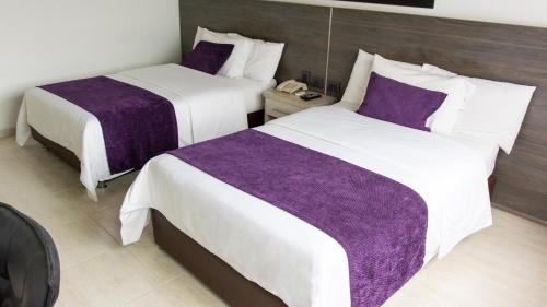 布卡拉曼加Hotel San Juan Internacional的两张位于酒店客房的床铺,配有紫色床单