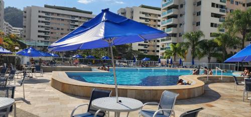 里约热内卢Apartamento por temporada RJ próximo ao Riocentro, Parque Olímpico e Jeunesse Arena的一个带桌椅和蓝伞的游泳池