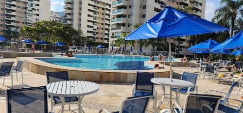 里约热内卢Apartamento por temporada RJ próximo ao Riocentro, Parque Olímpico e Jeunesse Arena的一个带桌椅和蓝伞的游泳池