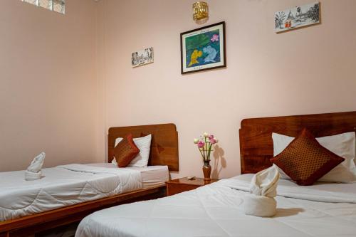 金边Nawin Palace Guesthouse的两张床铺,位于酒店客房,墙上挂着鲜花