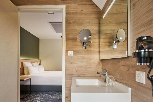 Évaux-les-BainsLe Grand Hôtel, The Originals Relais的一间带水槽的浴室和一张位于客房内的床