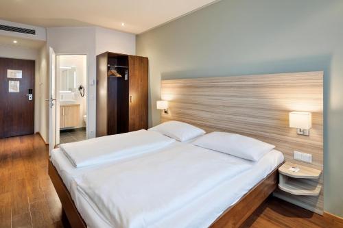 萨尔茨堡Austria Trend Hotel Salzburg Messe的卧室配有一张白色大床和木制床头板
